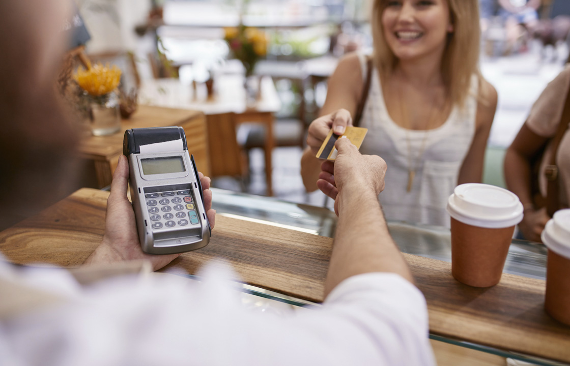 Femme à un comptoir de café, remettant avec le sourire sa carte de débit à la caissière