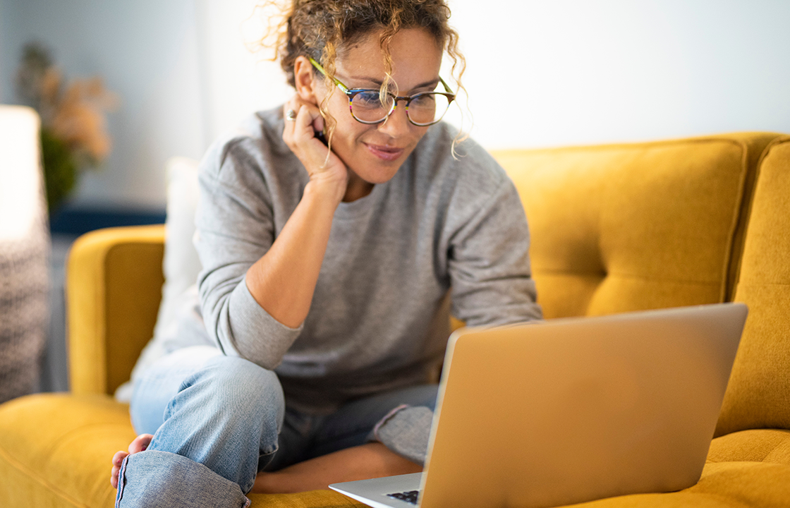 Une femme assise sur le canapé regarde son ordinateur portable